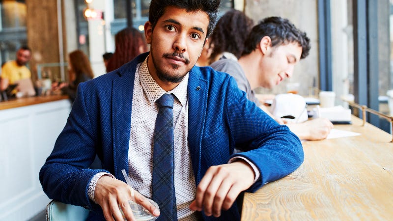 A man in a suit holds a coffee cup at a coffee shop
