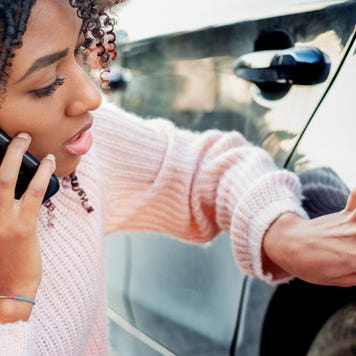 Younger black lady looking at damage to her car and talking on her phone to her insurance provider