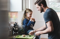 Side view of father cooking food while daughter having apple in kitchen