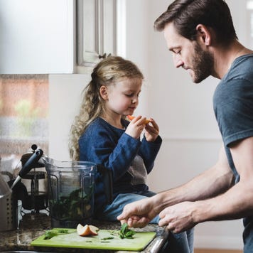 Side view of father cooking food while daughter having apple in kitchen