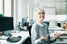 An older businesswoman sits smiling in an office