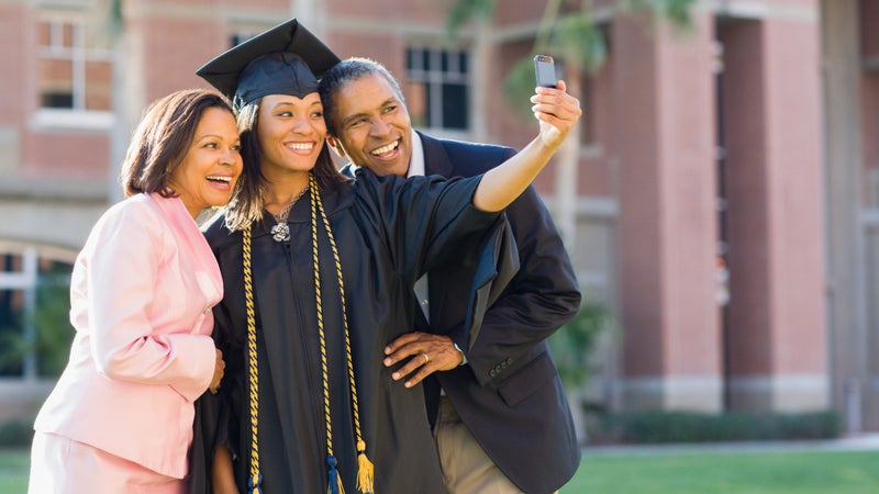 A young graduate woman takes a selfie with her parents