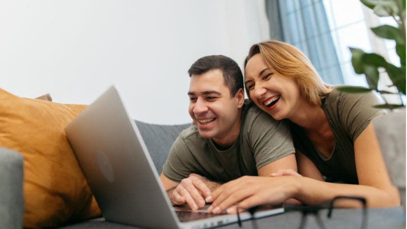 Newly married couple laugh together working on laptop