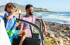 Man and boy look at beach while standing by car