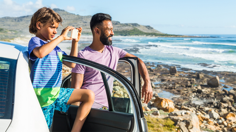 Man and boy look at beach while standing by car