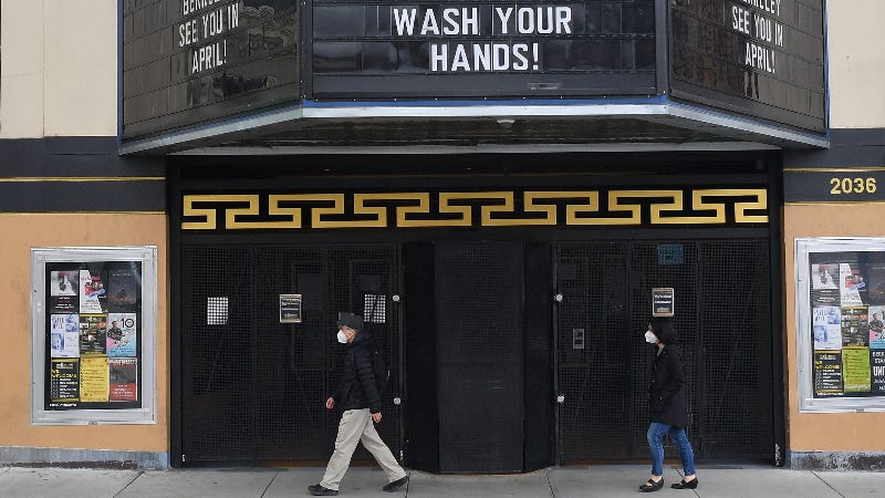 People wearing face masks walk in front of a closed theatre.