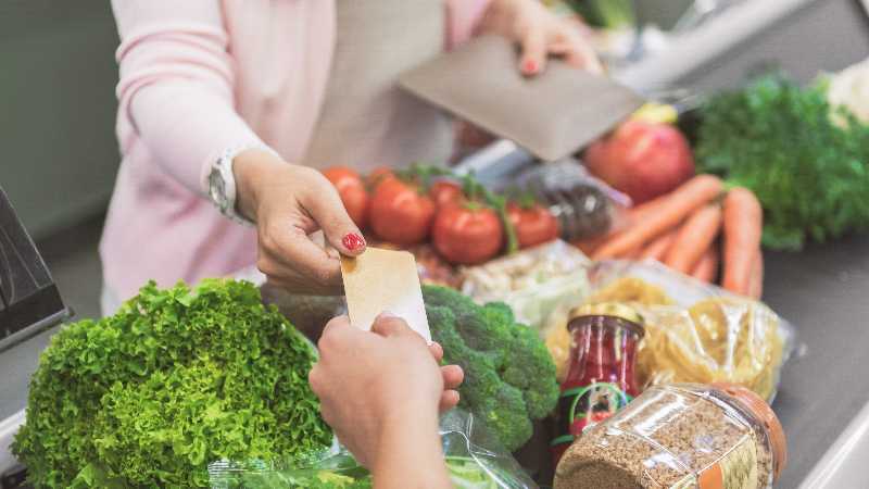 woman hands credit card to cashier at grocery store checkout