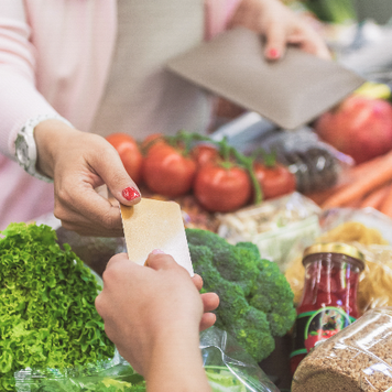 woman hands credit card to cashier at grocery store checkout