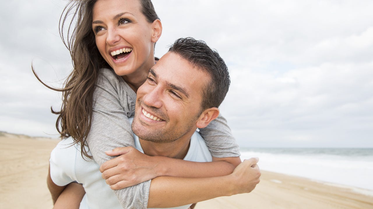 A young white couple walk along a sandy white beach