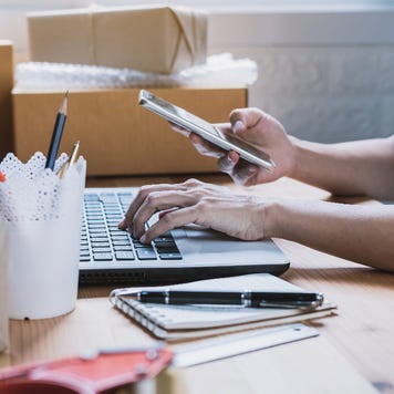 person with laptop looking at cell phone, surrounded by boxes