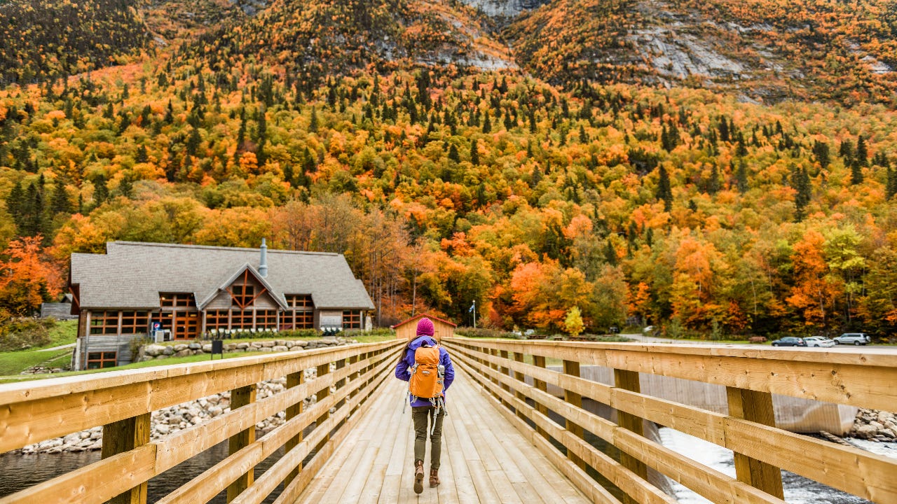 hiker walking across bridge towards cabin and mountains in autumn