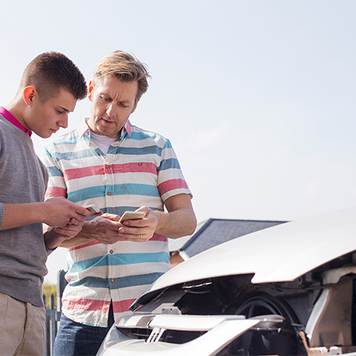 Two people looking at phone in front of damaged car