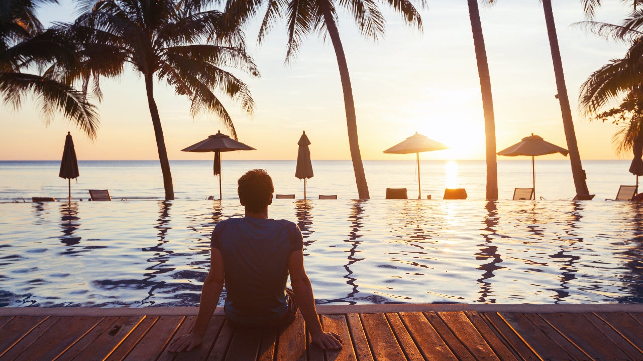 uomo seduto sul bordo di una piscina che guarda l'oceano al tramonto