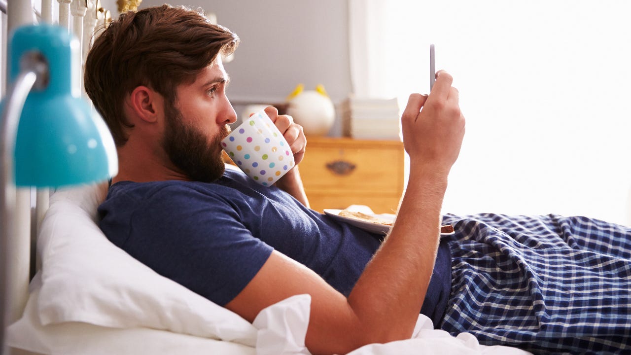 A man sits in bed, looking at his phone.