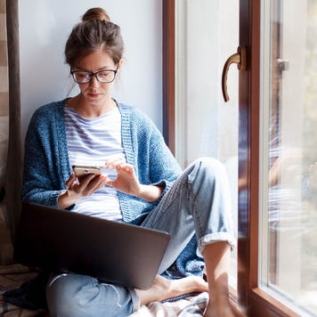 woman sitting at home looking at phone with laptop