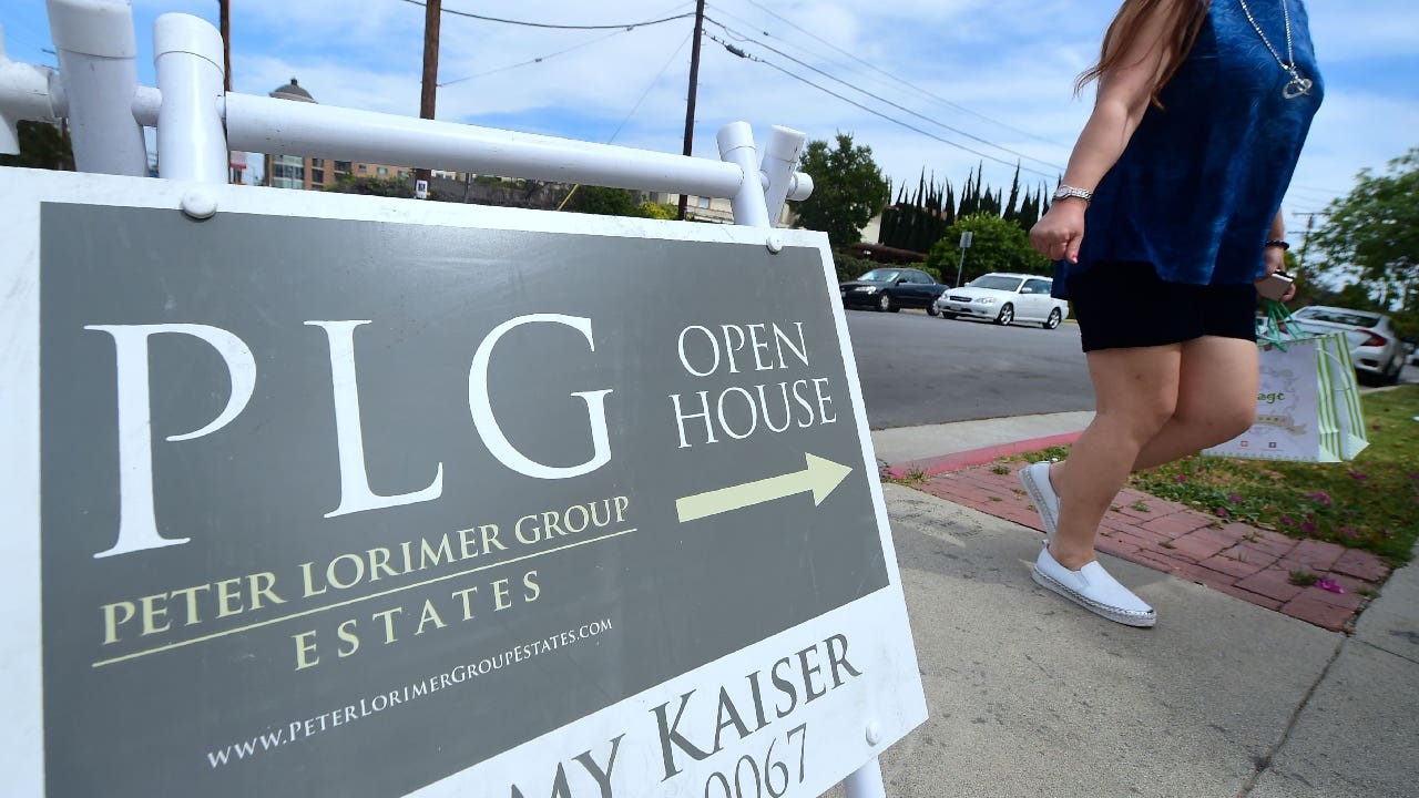 Woman walks past an open house sign.