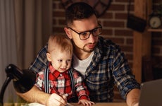 man working at laptop at home with young boy on his lap