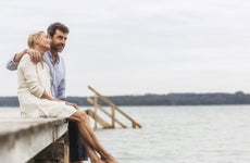 Older couple sitting together on a dock over a lake.