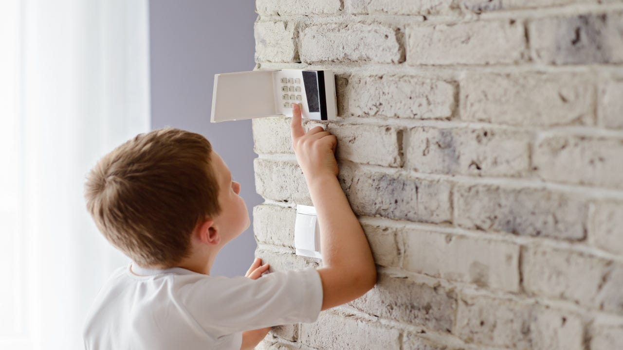 A boy reaching up to activate a home security system keypad.