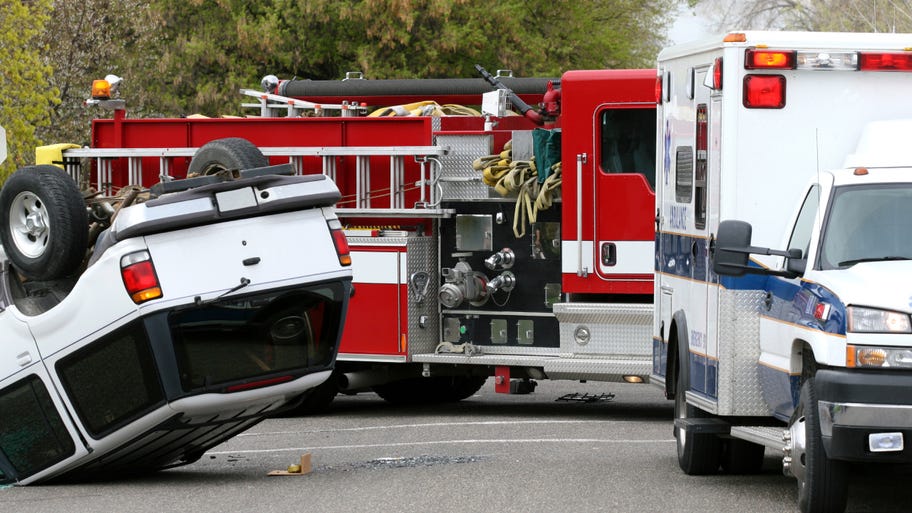 A car flipped over in the middle of the road next to an ambulance and firetruck.
