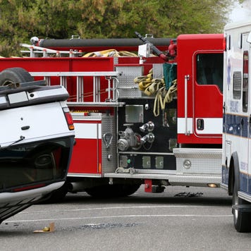 A car flipped over in the middle of the road next to an ambulance and firetruck.