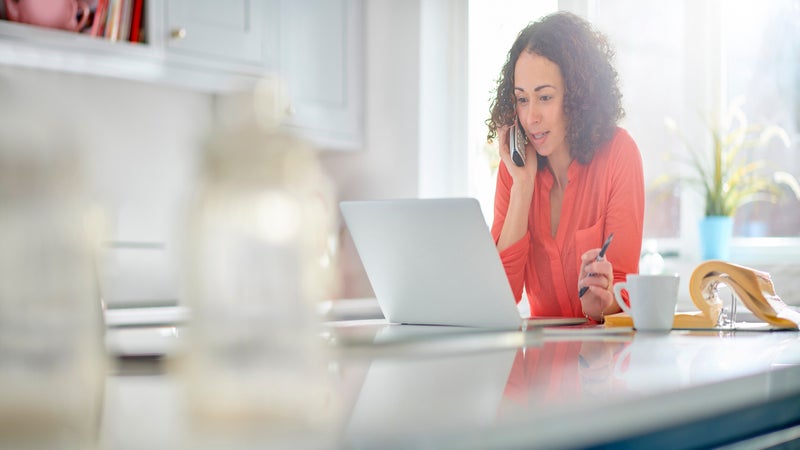 a woman  in her kitchen paying a bill by phone