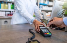 Wireless payment using smartphone and NFC technology. Close up. Male Customer paying with smart phone in pharmacy. Close Up shopping. Modern technology and people concept - Woman with payment terminal and male customer with smartphone paying for medications