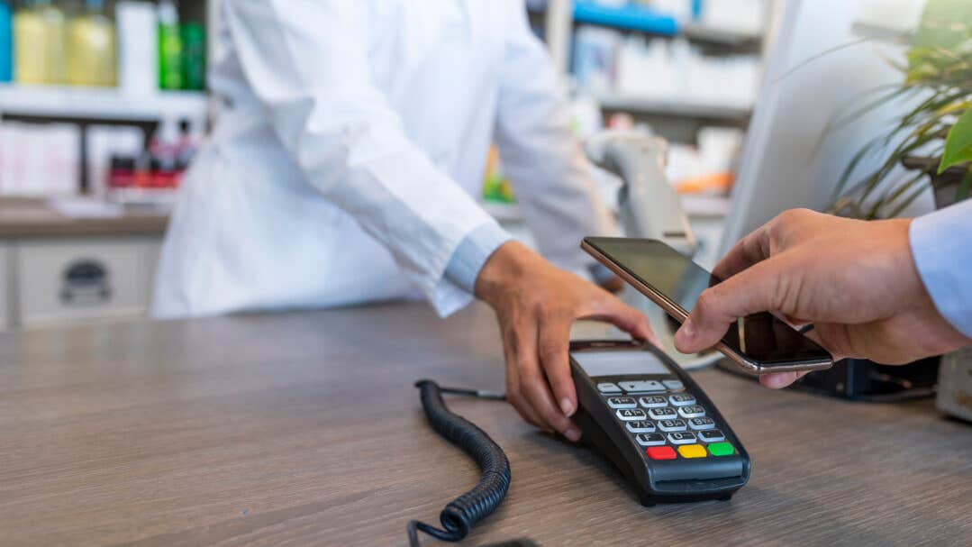 Wireless payment using smartphone and NFC technology. Close up. Male Customer paying with smart phone in pharmacy. Close Up shopping. Modern technology and people concept - Woman with payment terminal and male customer with smartphone paying for medications