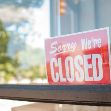A Sorry we're closed sign hands in a shop window