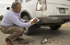 An older African American man assessing the damage to the back taillight of a car.