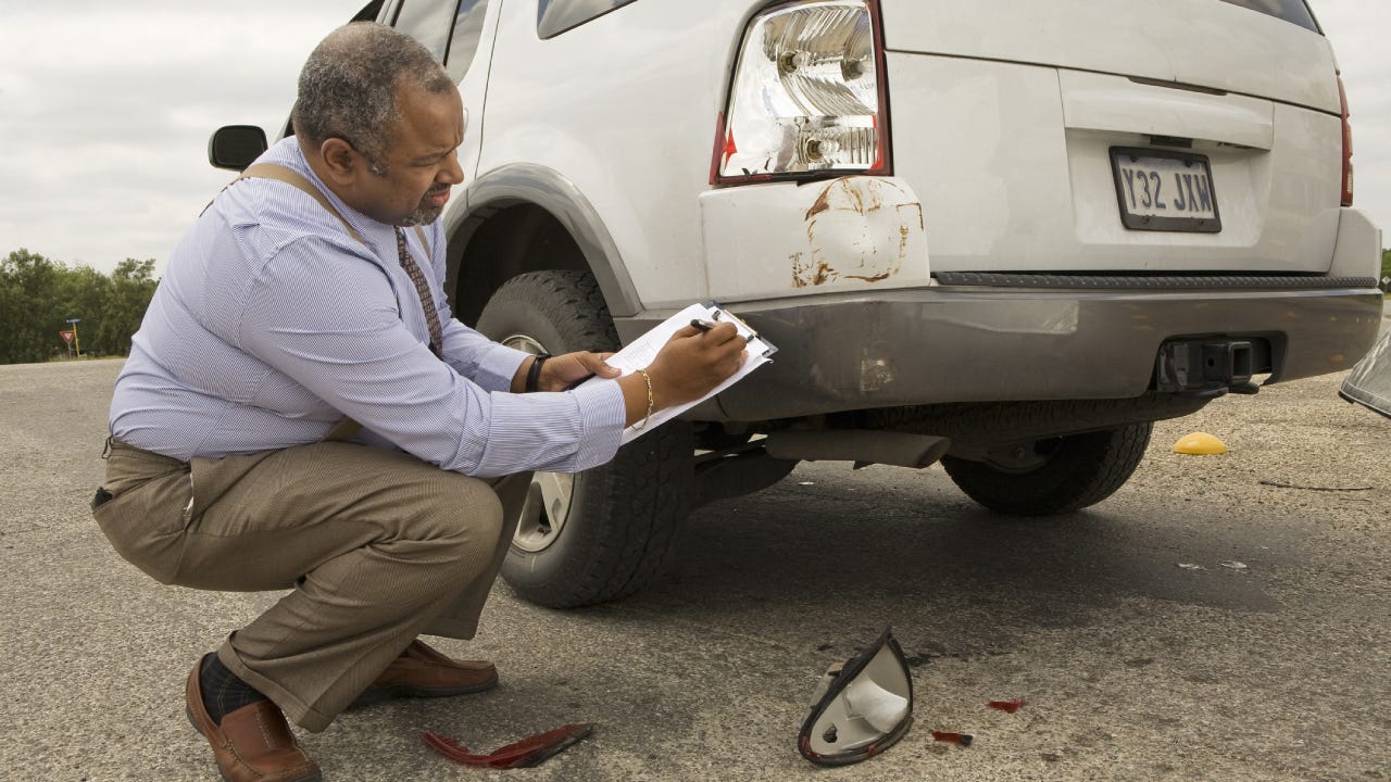 An older African American man assessing the damage to the back taillight of a car.