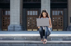 Student sitting on campus steps working on laptop.