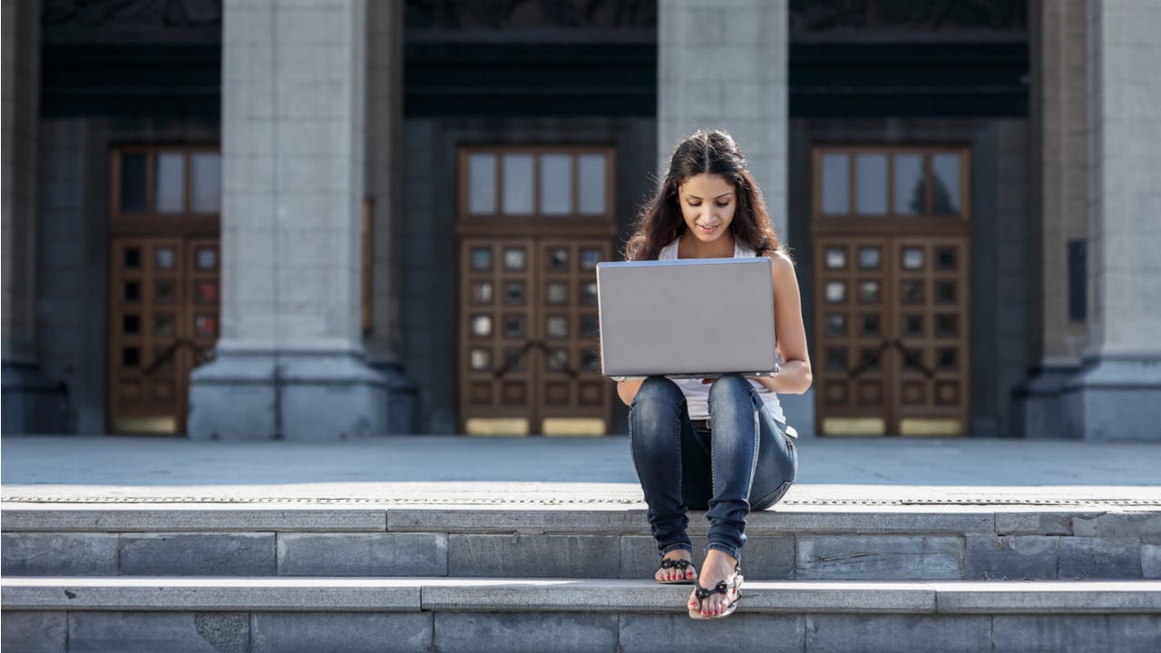 Student sitting on campus steps working on laptop.