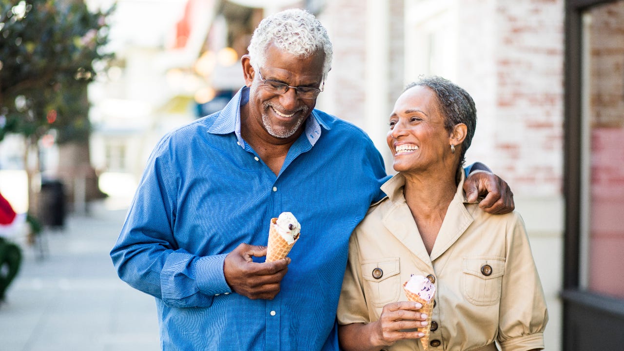 An older African-American couple walks together with ice cream cones