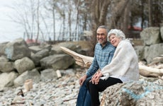 An older couple sitting together on a rocky beach.