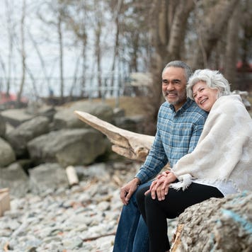An older couple sitting together on a rocky beach.
