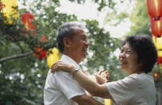 An older Asian couple dancing outdoors at a festival and laughing together.