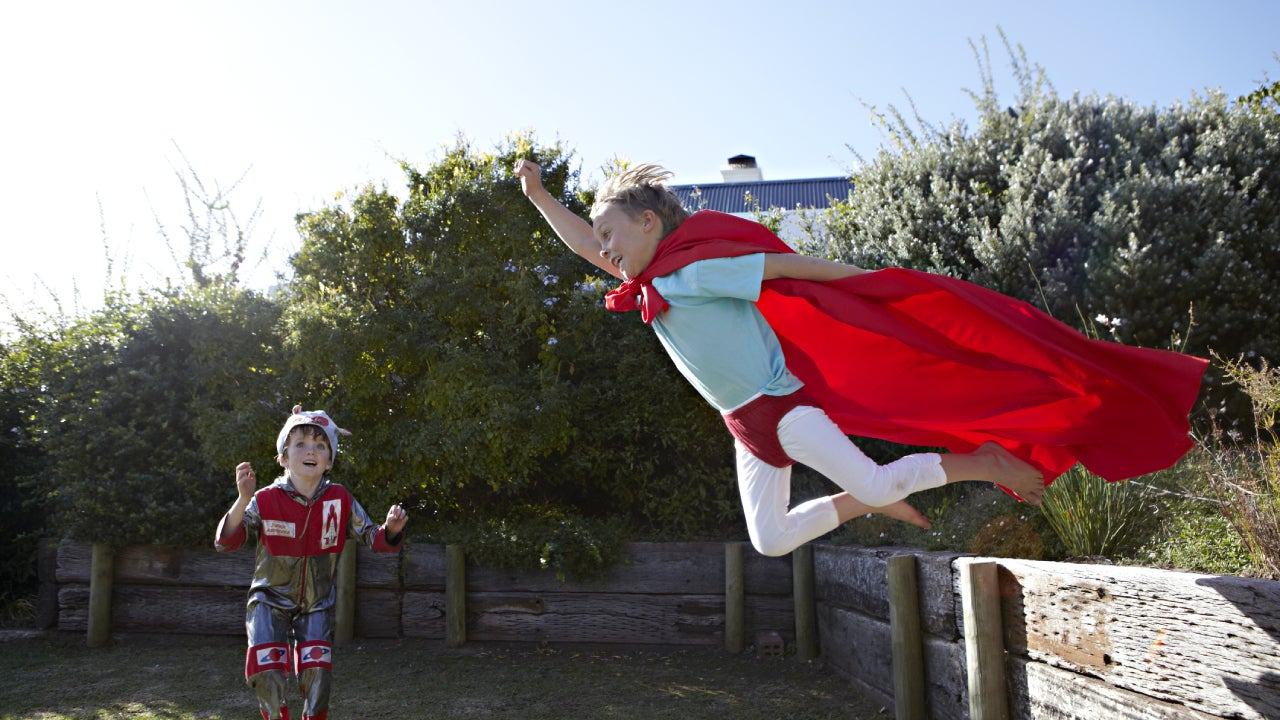 Two boys play superheroes out in the backyard.