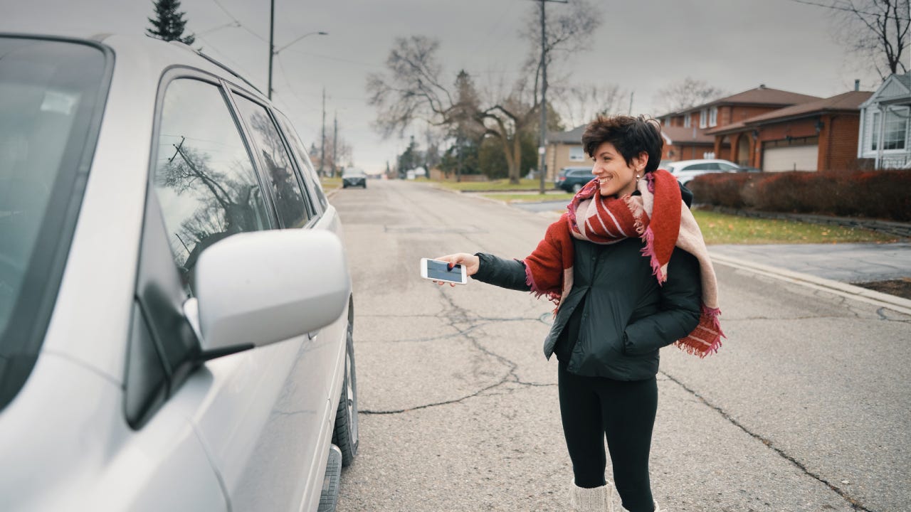 A woman stands outside of her smart car and activates it using her smartphone.