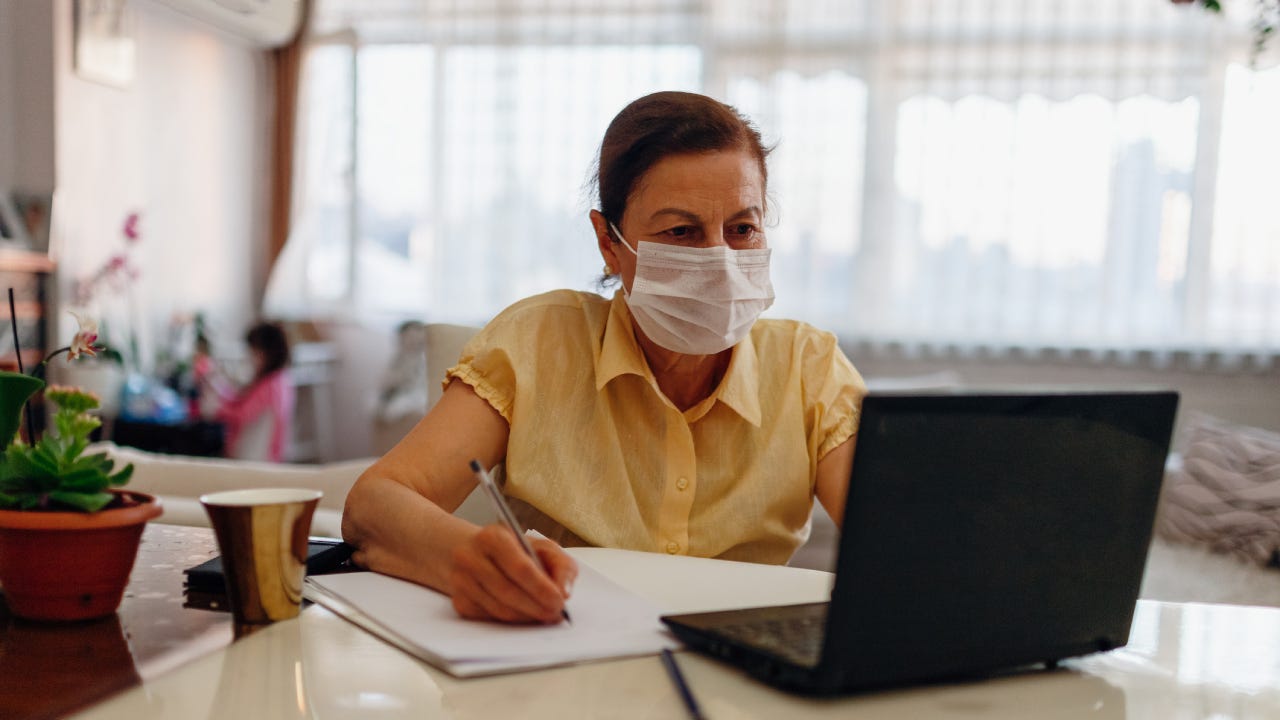 A woman wearing a facemask reviews her online information and accounts.