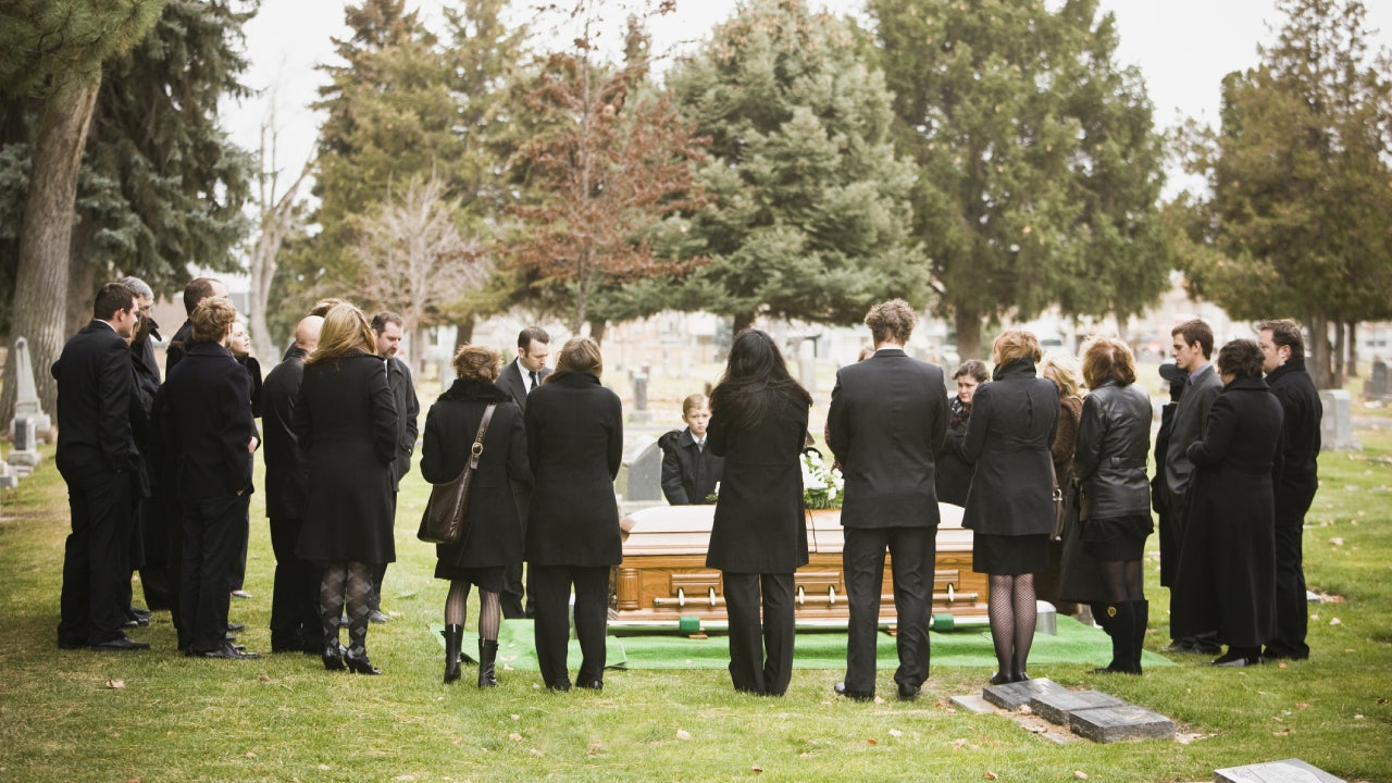 A group of people dressed up and standing around a coffin at a burial.