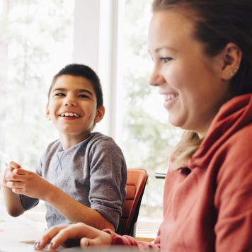 A mother sits at a computer while her special needs child sits next to her; they are laughing.