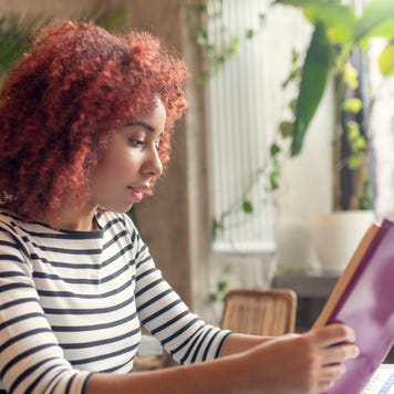 Young woman reads a book at her desk.