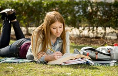 Student studying on grass on college campus.