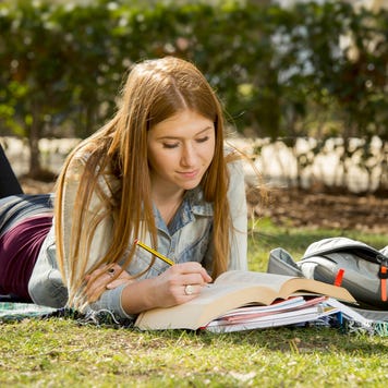 Student studying on grass on college campus.
