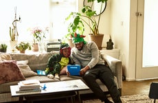 A father and his son, dressed up like dragons, do a learning exercise in the living room.