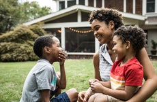 Single mother playing with young sons in front of house