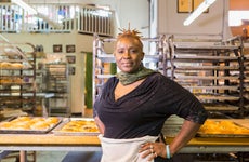 An older Black businesswoman stands in front of her kitchen