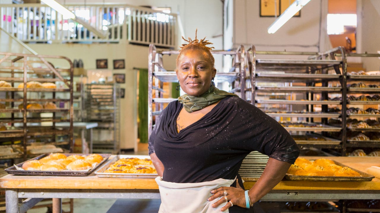 An older Black businesswoman stands in front of her kitchen