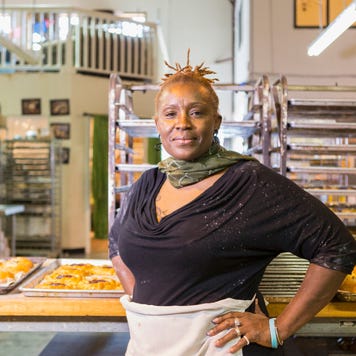 An older Black businesswoman stands in front of her kitchen